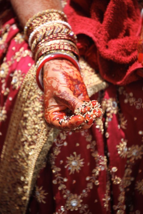 A bride's hennaed hand holding auspicious rice and flowers at a traditional Vaishnava wedding, used here to illustrate the marriage customs of Jayadeva and Padmavati's era.