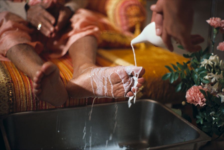 A close-up devotional photograph of charanamrita (water and milk poured over Deity feet) being collected, used on gaudiyahistory.iskcondesiretree.com's biography page for Kali Das — chosen for this page because it echoes the text's own desc