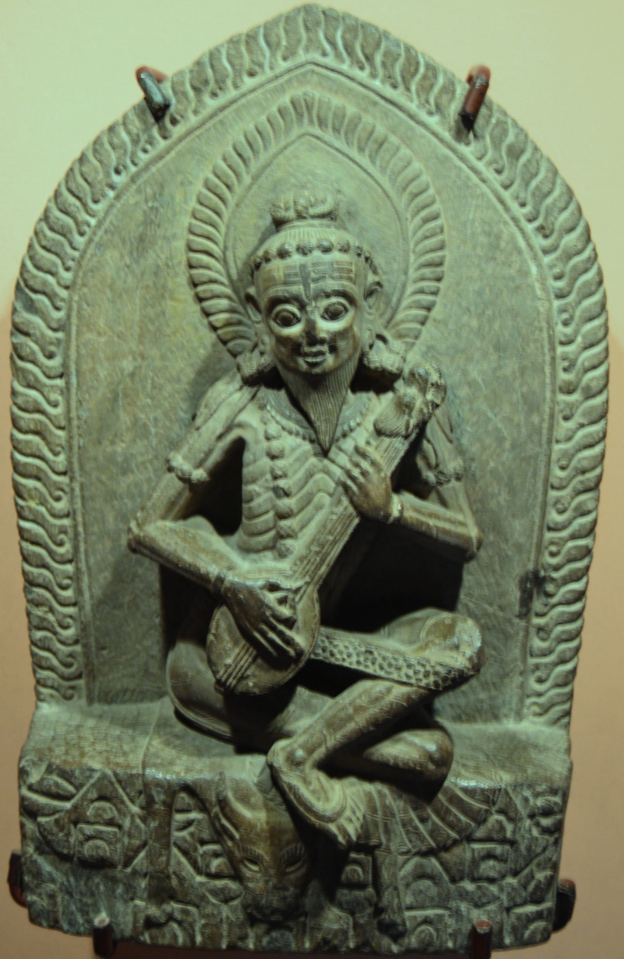 A carved stone relief of Narada Muni seated and playing the vina, photographed at a temple in Nepal.