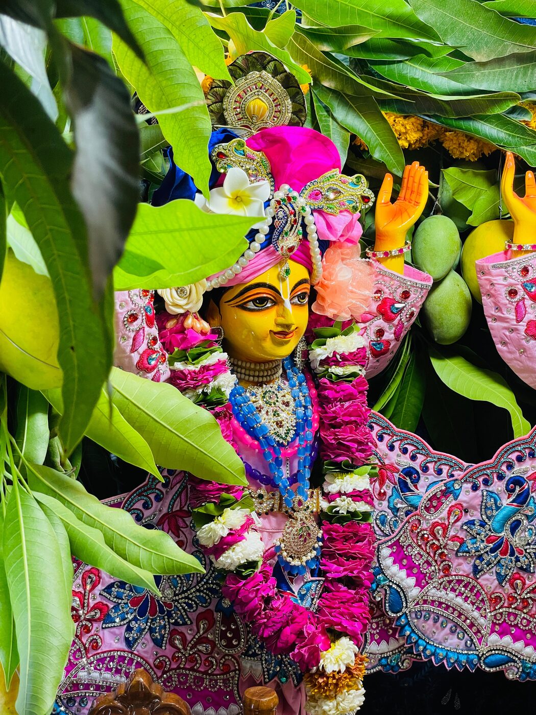 A garlanded deity of Sri Nityananda Prabhu decorated with mango leaves and fresh flowers for a festival.