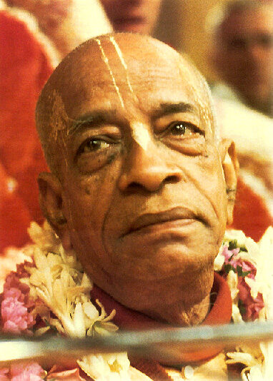 Close-up portrait of Srila Prabhupada wearing a flower garland, with a contemplative expression.