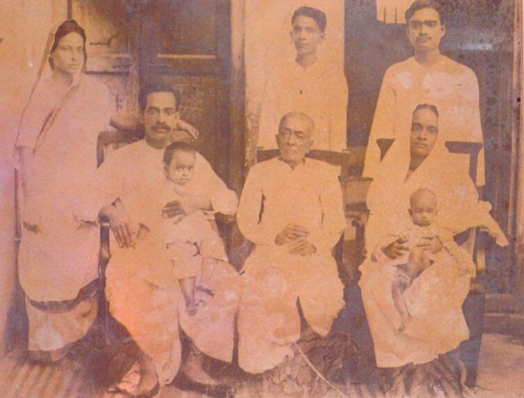 A rare, faded family photograph from Srila Prabhupada's householder years in Calcutta, showing him as a young family man (Abhay Charan De) together with members of his extended family and small children.