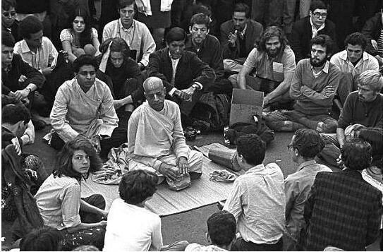 Srila Prabhupada seated on the ground in conversation with a circle of young Western followers in the early days of ISKCON.