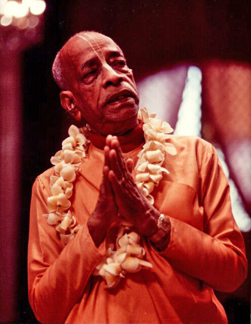 Srila Prabhupada with hands folded in a gesture of greeting and prayer, wearing a flower garland; one of the most widely reproduced portraits of him.