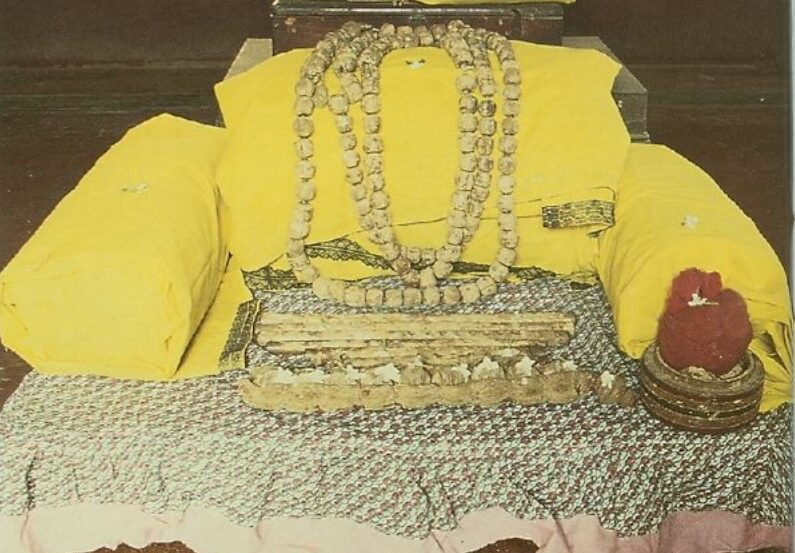 Altar display of preserved relics including a palm-leaf Bhagavad-gita, flutes, and beads